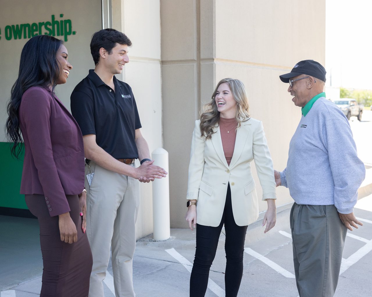 Four Enterprise Mobility team members talking and laughing in front of a local neighborhood retail branch. 