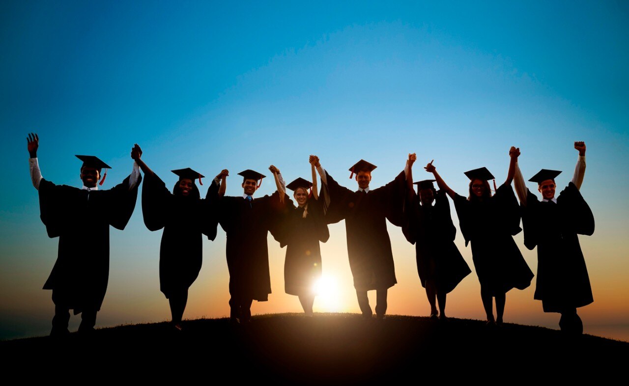 Students in graduation caps and gowns walking into the sunset