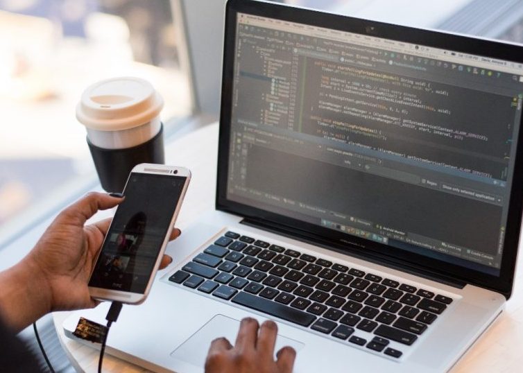 Persona que mira el MacBook mientras usa su teléfono móvil