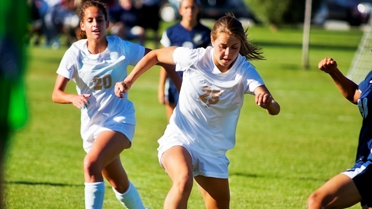 Chicas jugando al fútbol con uniformes blancos