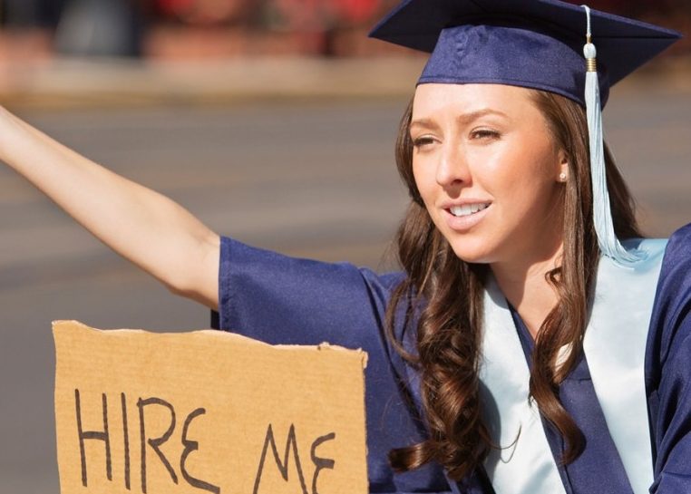 Estudiante con gorra y bata de graduación con cartel de cartón que dice "Arrendame"