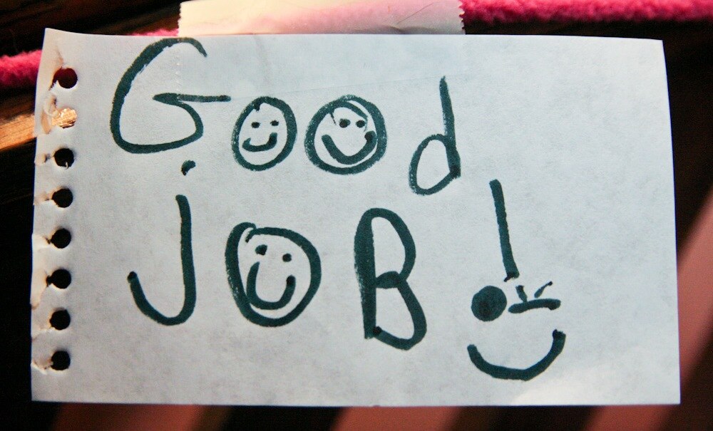 Pieza de papel de cuaderno que dice "buen trabajo" con caras sonrientes