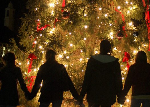 Gente que se toma de la mano frente a un árbol de Navidad