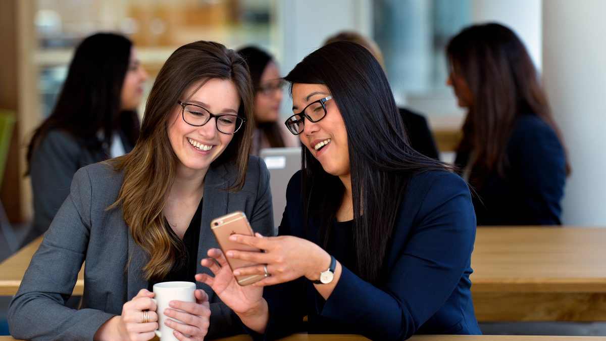 Dos mujeres sonriendo y mirando un teléfono móvil