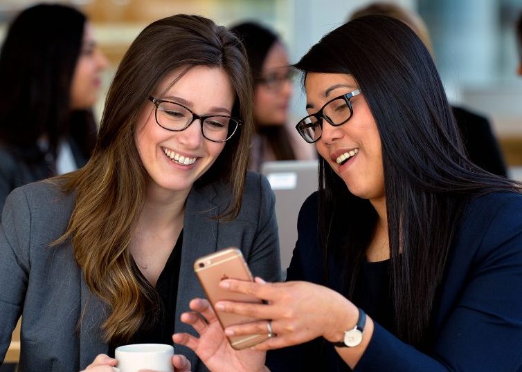 Dos mujeres sonriendo y mirando un teléfono móvil