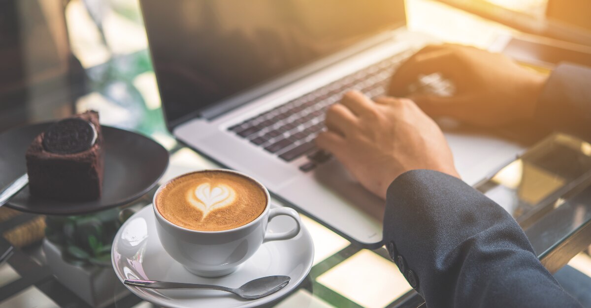 Escribir con las manos en un MacBook con café y pastel en la mesa