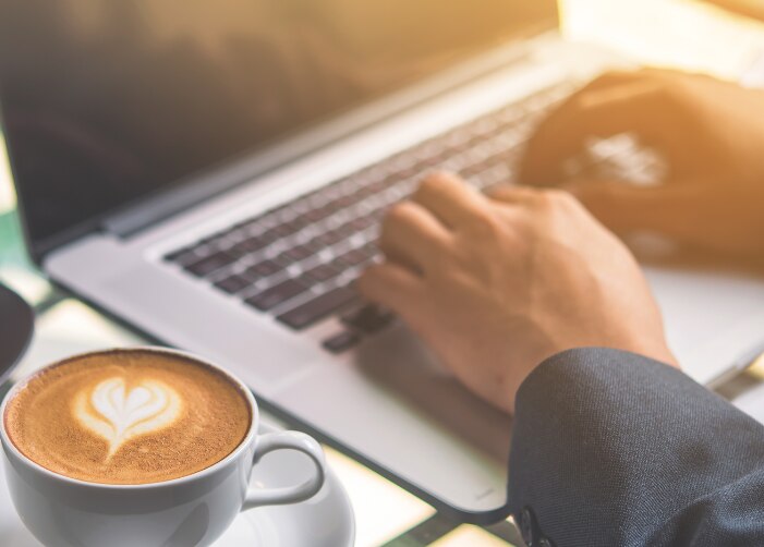 Escribir con las manos en un MacBook con café y pastel en la mesa