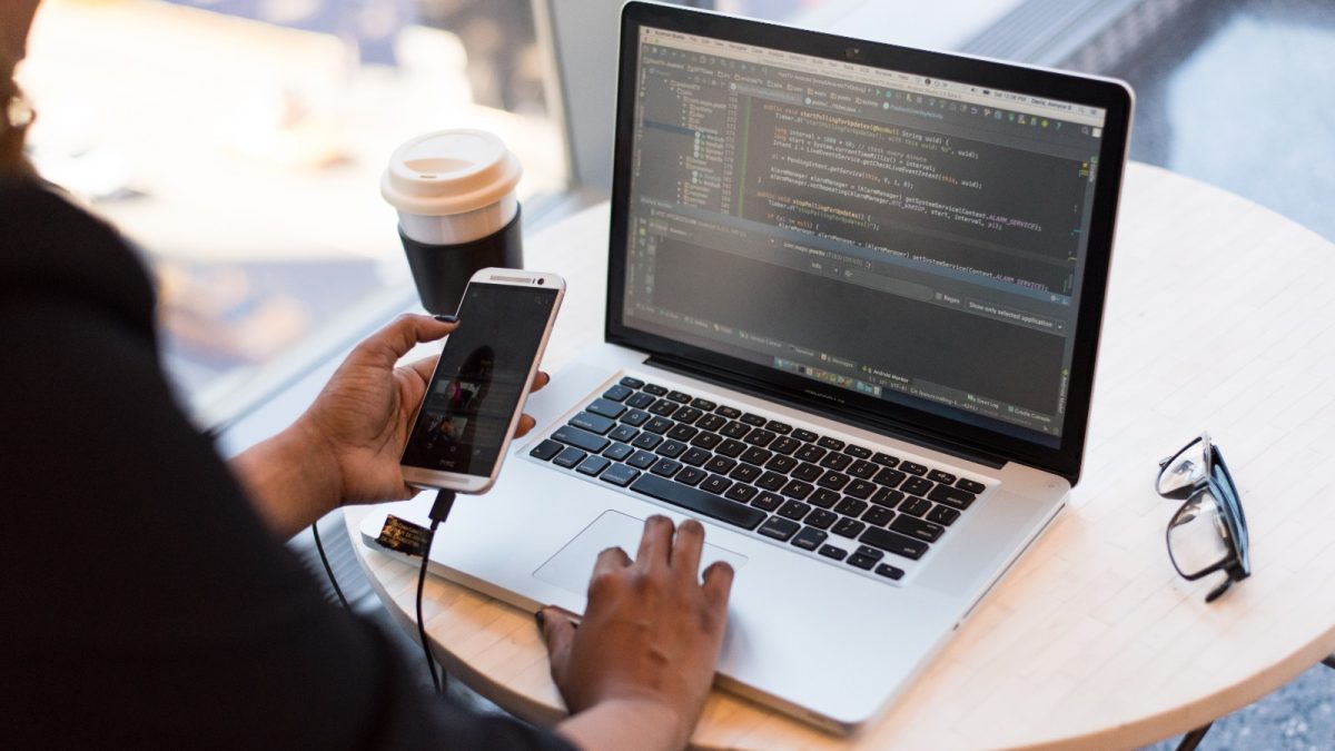 Persona que mira el MacBook mientras usa su teléfono móvil