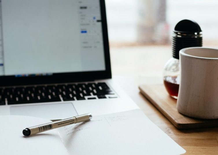 Abra el portátil y el portátil con bolígrafo y taza de café en el escritorio
