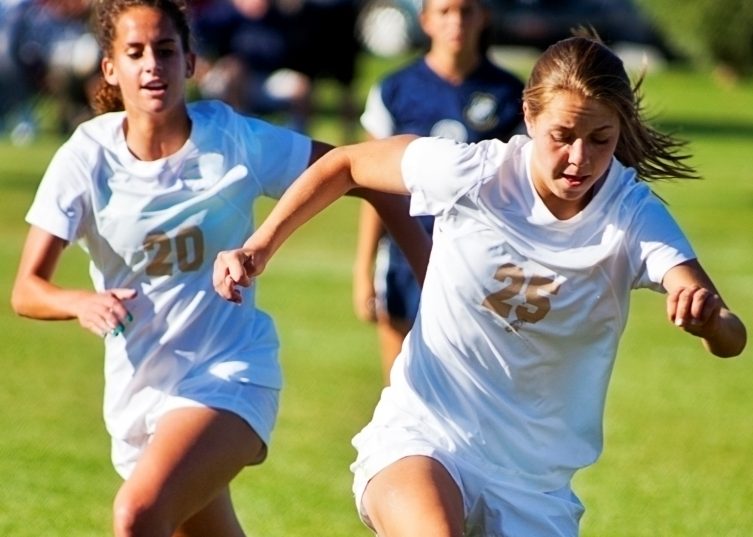 Chicas jugando al fútbol con uniformes blancos