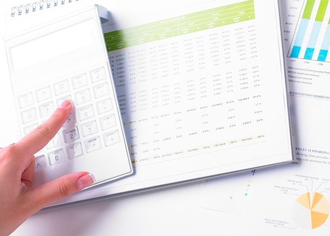 El dedo usa la calculadora mientras que la otra mano sostiene un bolígrafo que apunta a un gráfico