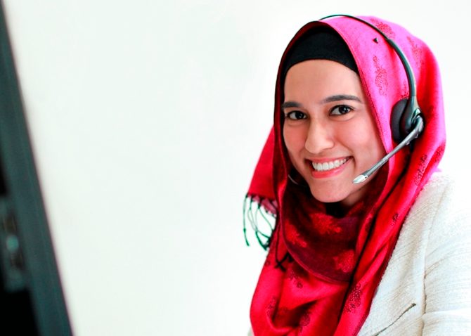 Señora sonriente que trabaja desde casa con un auricular sentado en un ordenador