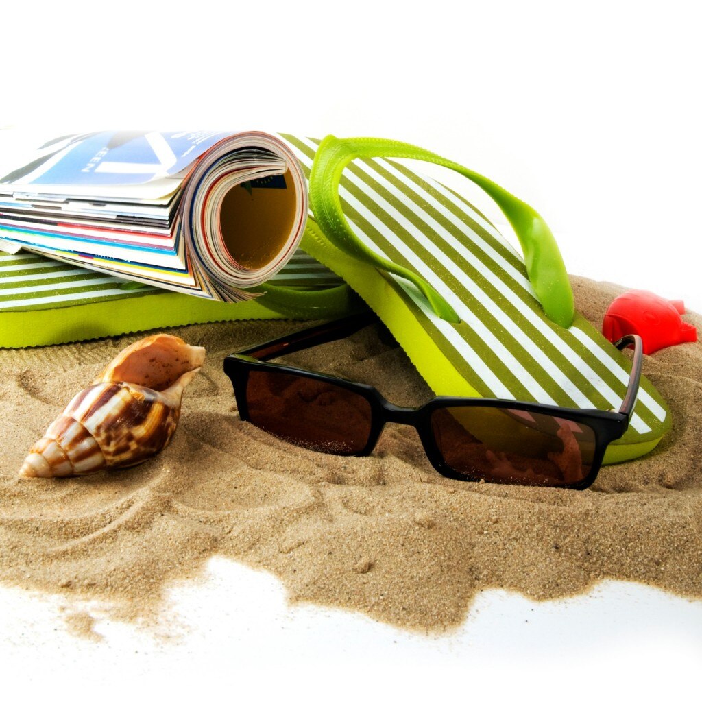 Gafas de sol, una revista, sandalias y una concha marina en la playa
