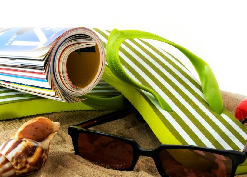 Gafas de sol, una revista, sandalias y una concha marina en la playa
