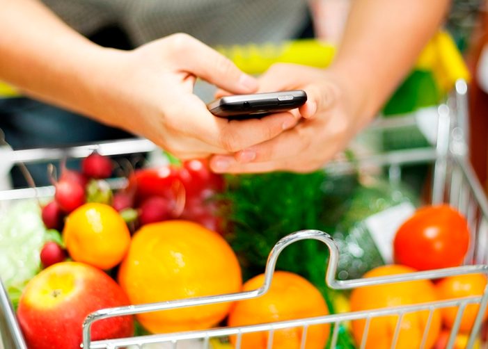 Enviar mensajes de texto mientras empuja el carrito de compras lleno de frutas y verduras
