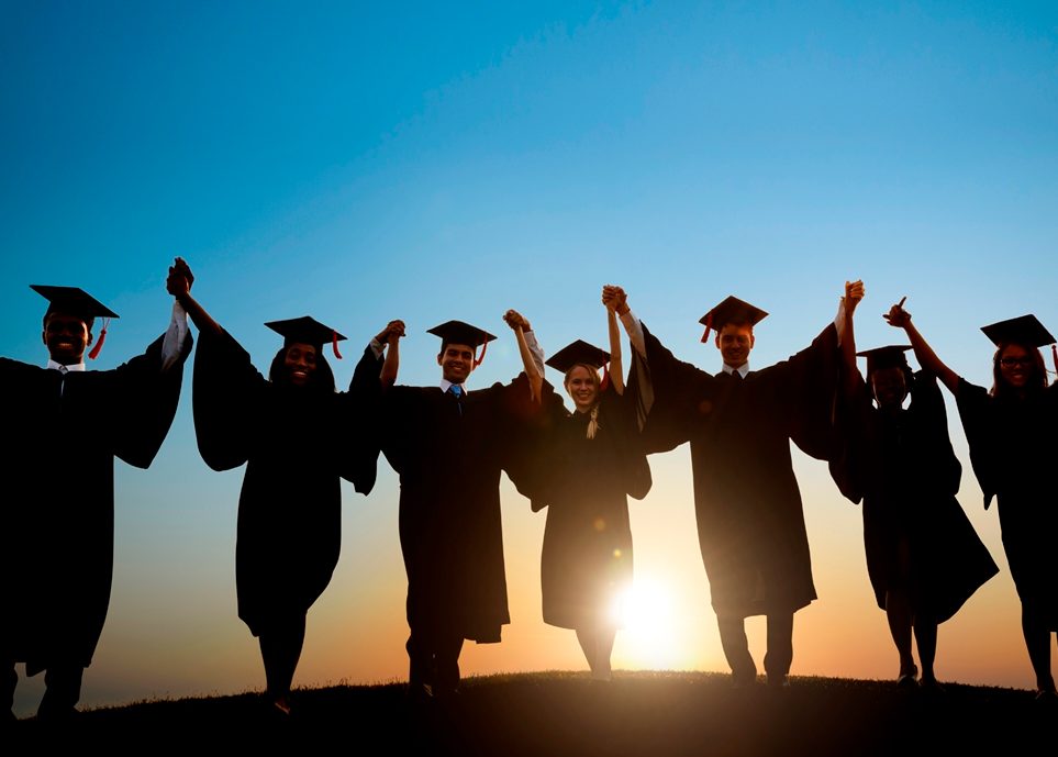 Estudiantes con gorros y batas de graduación caminando hacia la puesta de sol
