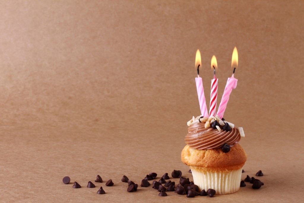 Cupcake con tres velas encendidas rodeadas de chispas de chocolate