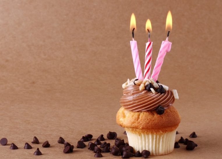 Cupcake con tres velas encendidas rodeadas de chispas de chocolate