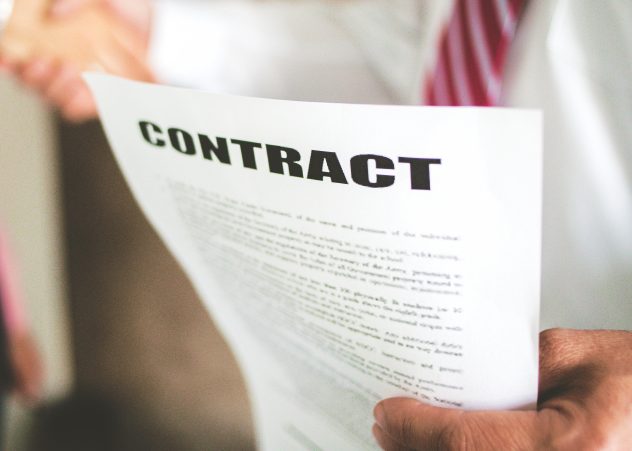 Gente borrosa dándole la mano con un papel que dice "Contrato" en el centro de atención