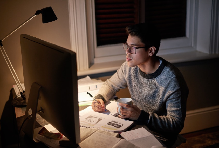 Estudiante revisando un documento tarde por la noche en el brillo de la pantalla de una computadora