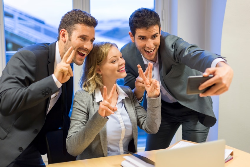 3 personas haciendo señales de paz mientras se toman un selfie con ropa profesional