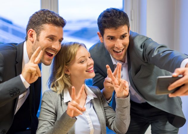 3 personas haciendo señales de paz mientras se toman un selfie con ropa profesional