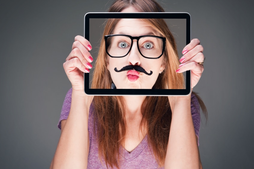 Chica sosteniendo el iPad frente a su cara con una foto de su cara con un bigote falso y gafas