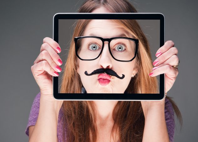 Chica sosteniendo el iPad frente a su cara con una foto de su cara con un bigote falso y gafas