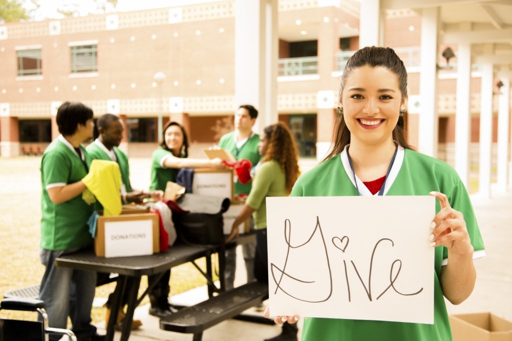 Muchacha sosteniendo un cartel que dice "dar" mientras que los amigos empacan cajas de donaciones