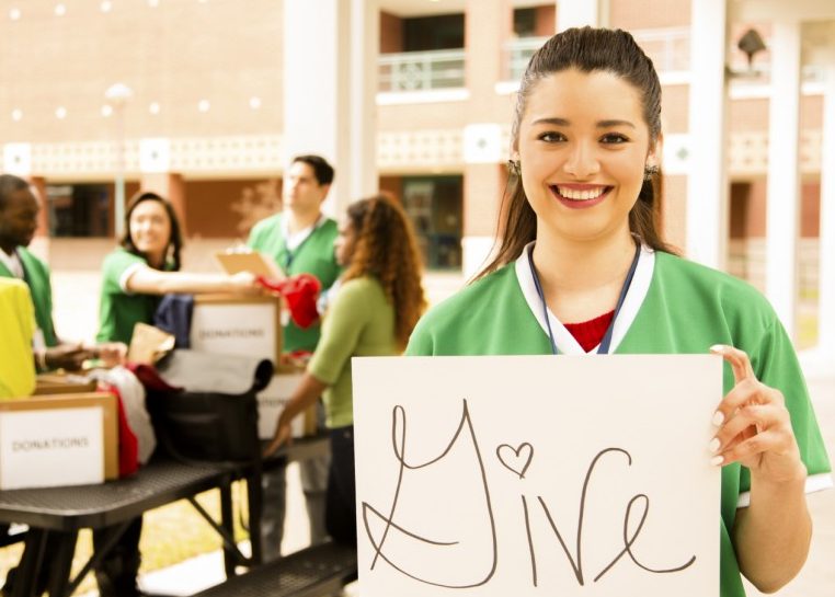 Muchacha sosteniendo un cartel que dice "dar" mientras que los amigos empacan cajas de donaciones