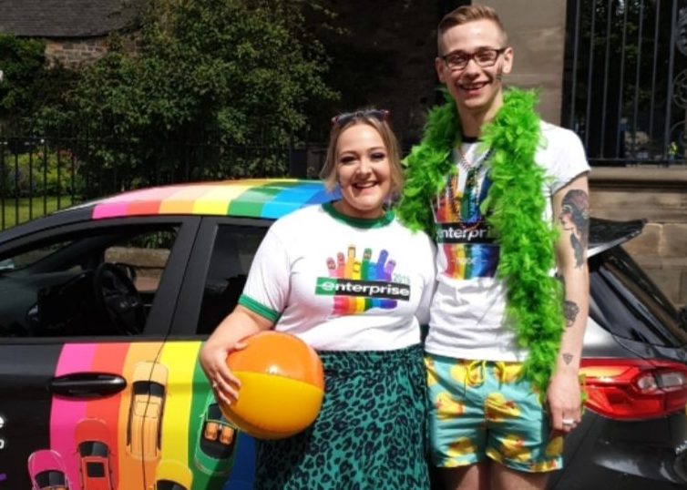 Dylan con otro empleado de Enterprise en un evento PRIDE con el vehículo PRIDE de Enterprise