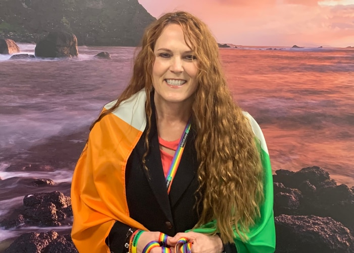 Leslee con bandera irlandesa alrededor de sus hombros frente al océano