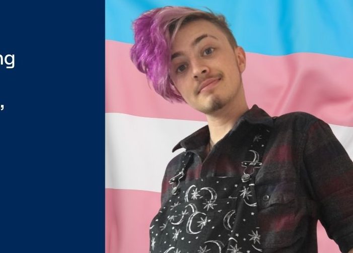 Foto de Jay delante de una bandera azul, rosa y blanca con cita sobre fondo azul