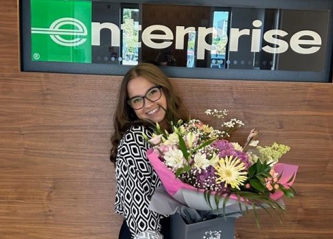 Foto de Yasmin con flores delante del cartel de Enterprise con cita