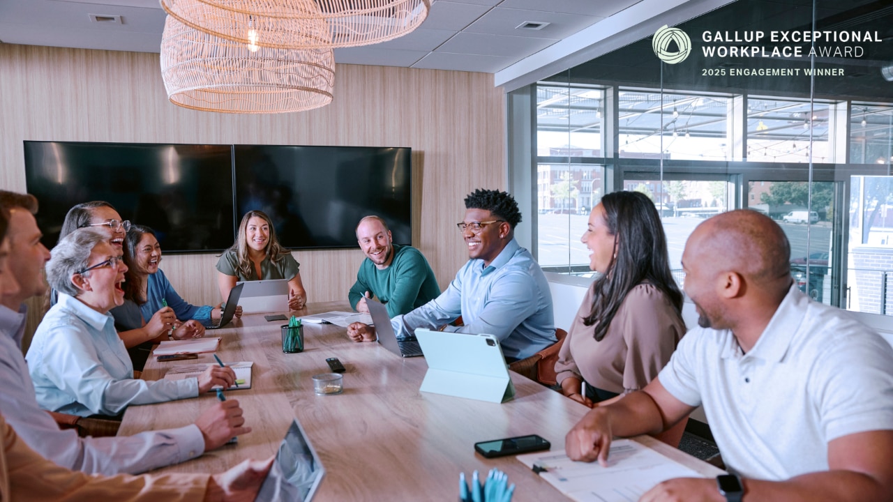 Enterprise mobility team members in workplace sitting around a table talking with Gallup Exceptional Workplace award logo..