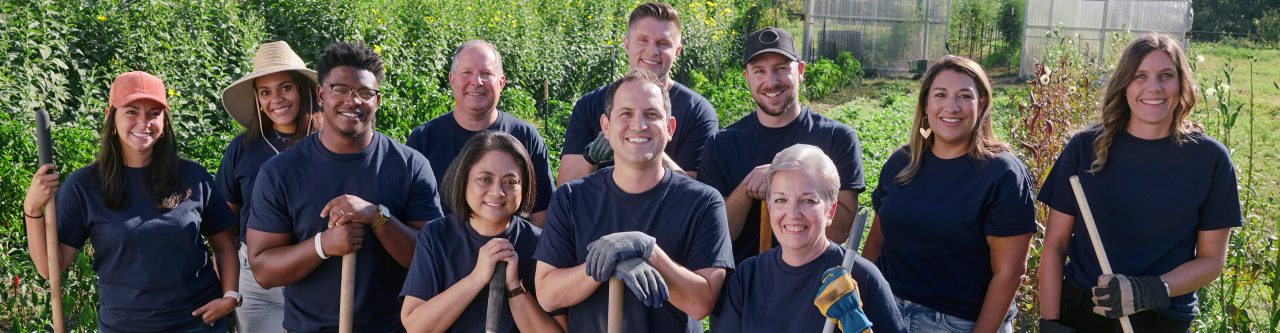 Un grupo de sonrientes miembros del equipo de Enterprise Mobility con palas y rastrillos en un campo soleado 