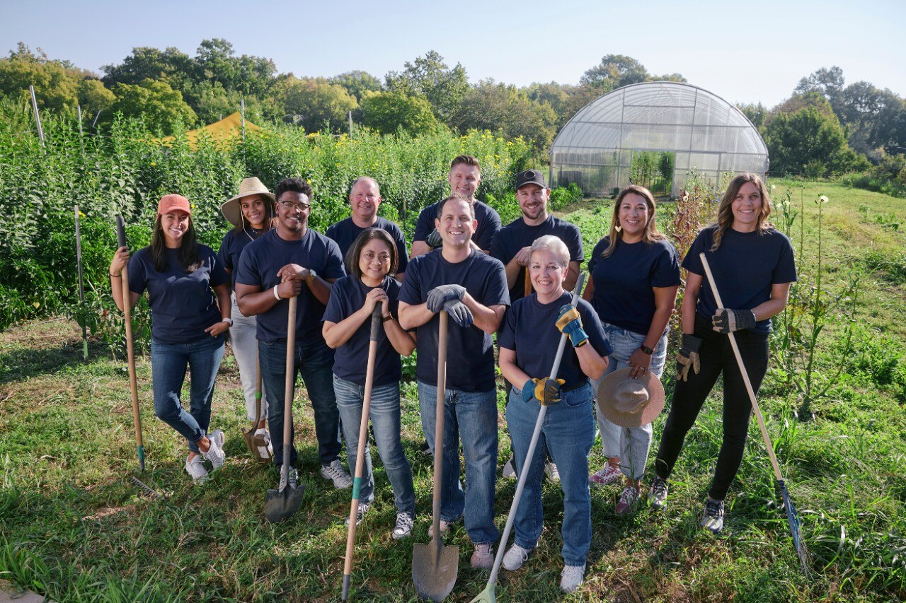 Un grupo de sonrientes integrantes del equipo de Enterprise Mobility con palas y rastrillos en un campo soleado