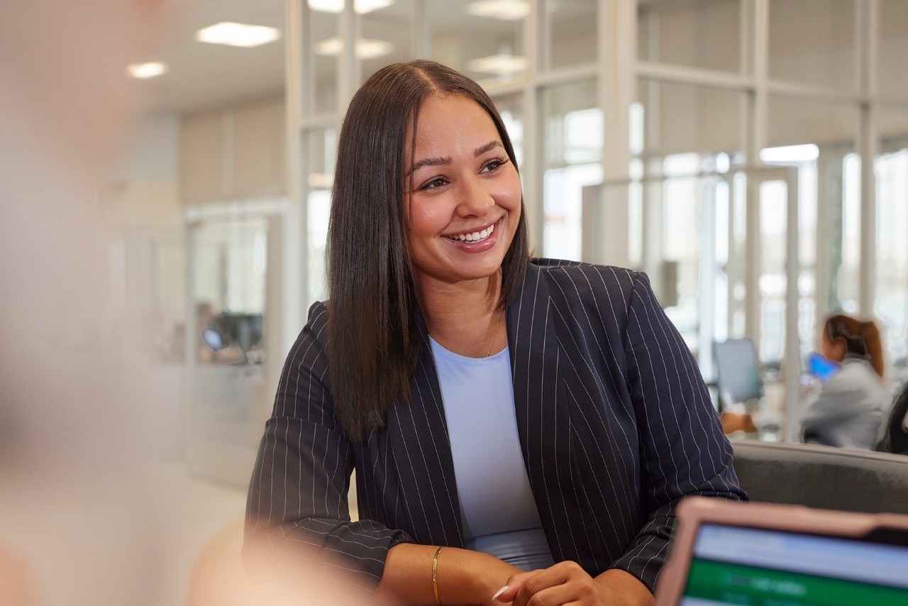 Miembro del equipo de Enterprise Mobility sentado en un escritorio sonriendo a la persona que está sentada a su lado. 