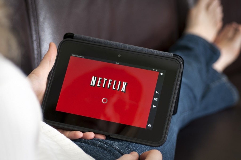 Tableta con Netflix en ella sostenida por una persona sentada en el sofá con las piernas cruzadas