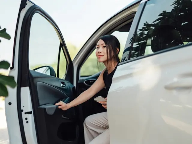 Mujer joven saliendo del asiento del conductor de un monovolumen blanco.